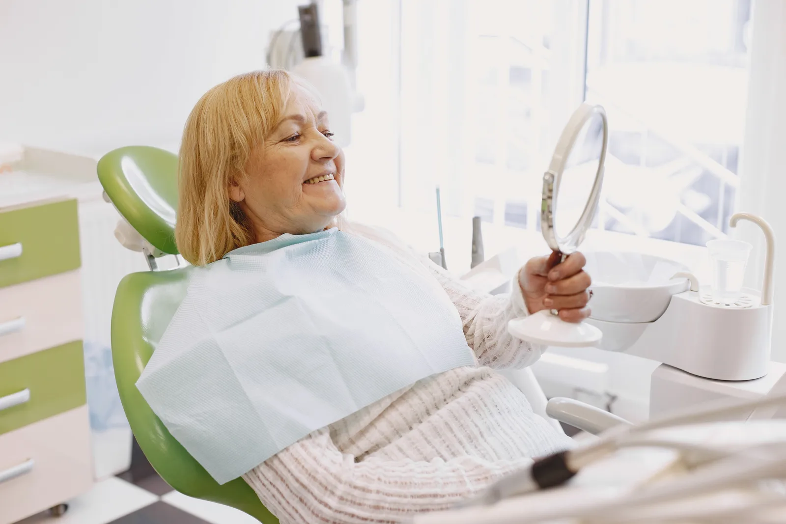 Patient reviewing a new smile in the mirror, shown while covering Full Mouth Cost in Winnipeg